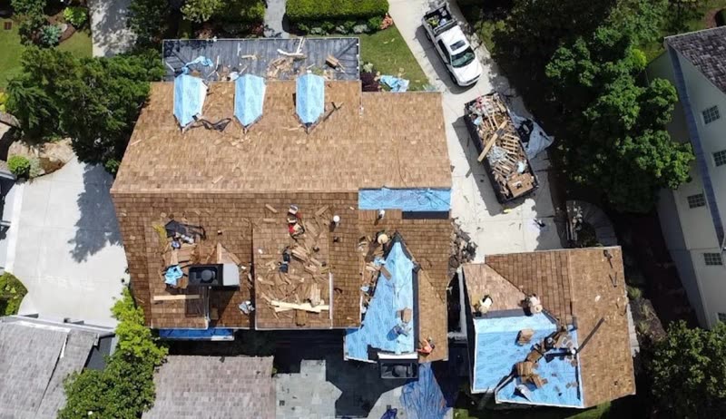 Cedar shake tear-off in progress, tarps protecting the property and a debris trailer in the drive
