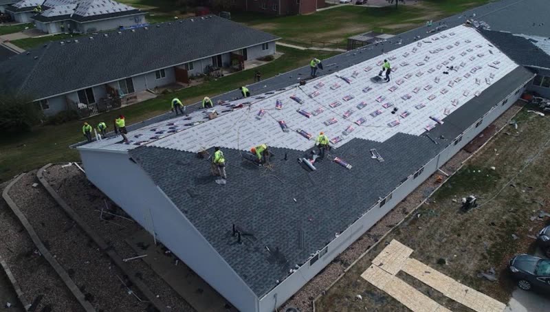 Roofing crew installing architectural shingles over synthetic underlayment on a long multifamily building
