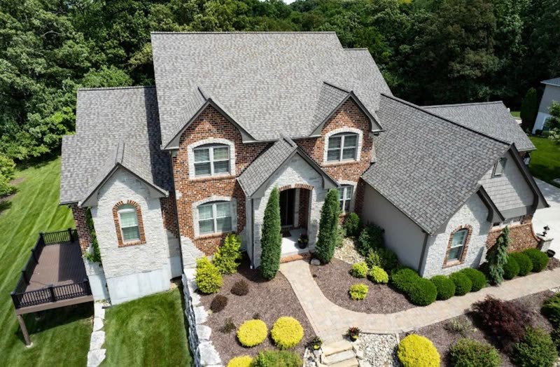 The same brick and stone home finished, new shingle roof complete and the site cleared