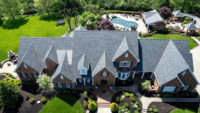 Aerial front elevation of a brick estate with multiple gables and a new shingle roof