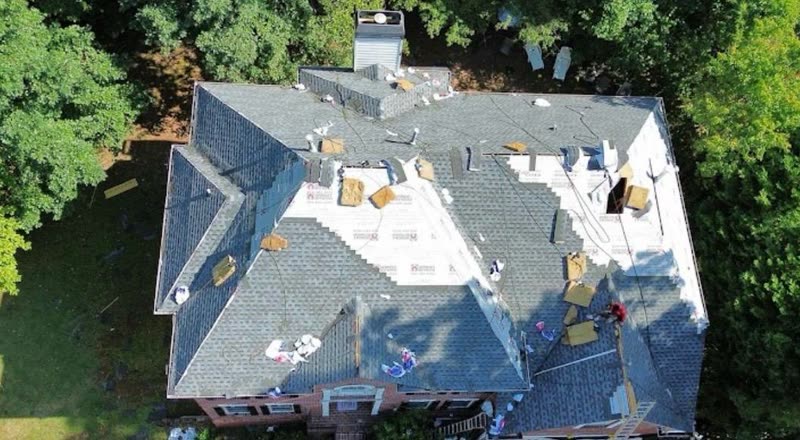 Underlayment down and shingle bundles staged across a large estate roof mid installation
