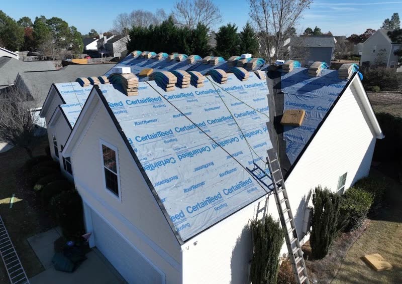 House dried in with underlayment and shingle bundles staged along the ridge