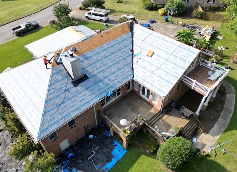 House fully dried in with underlayment after tear-off, tarps protecting the deck and yard