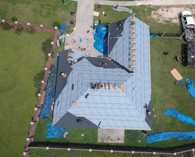 Long roof dried in with underlayment, tarps laid out across the yard for debris