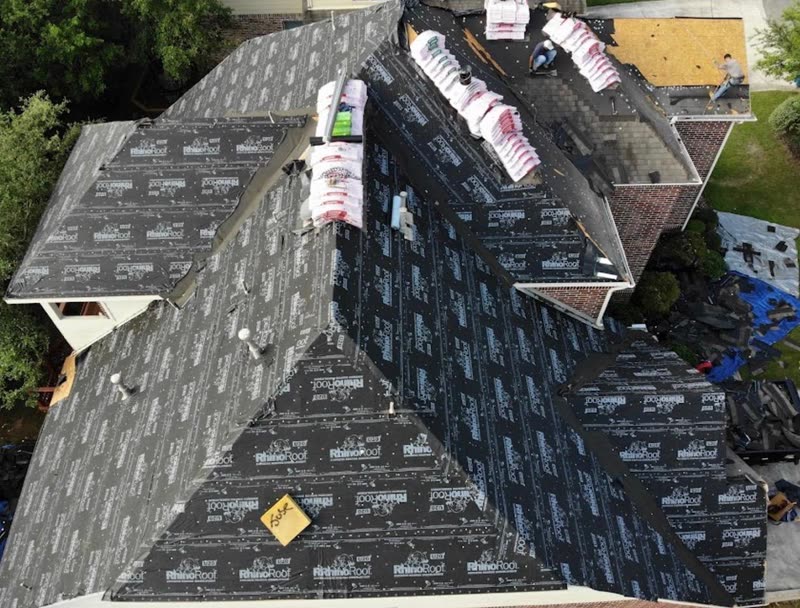 Synthetic underlayment installed across a house roof with shingle bundles staged on the ridge